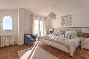 A bedroom with a large bed, a chair, a window, and a decorative wall piece.