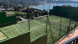 A tennis court with a view of a coastal town and mountains in the background.