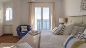 A hotel room with a bed, a chair, a view of the sea, and a radiator.