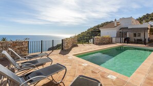 A swimming pool with lounge chairs, a stone wall, and a view of the sea.