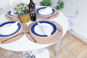 Uma mesa redonda com quatro jogos americanos azul e castanho, uma garrafa de vinho Don Simon Tempranillo e uma cesta de palha com flores.