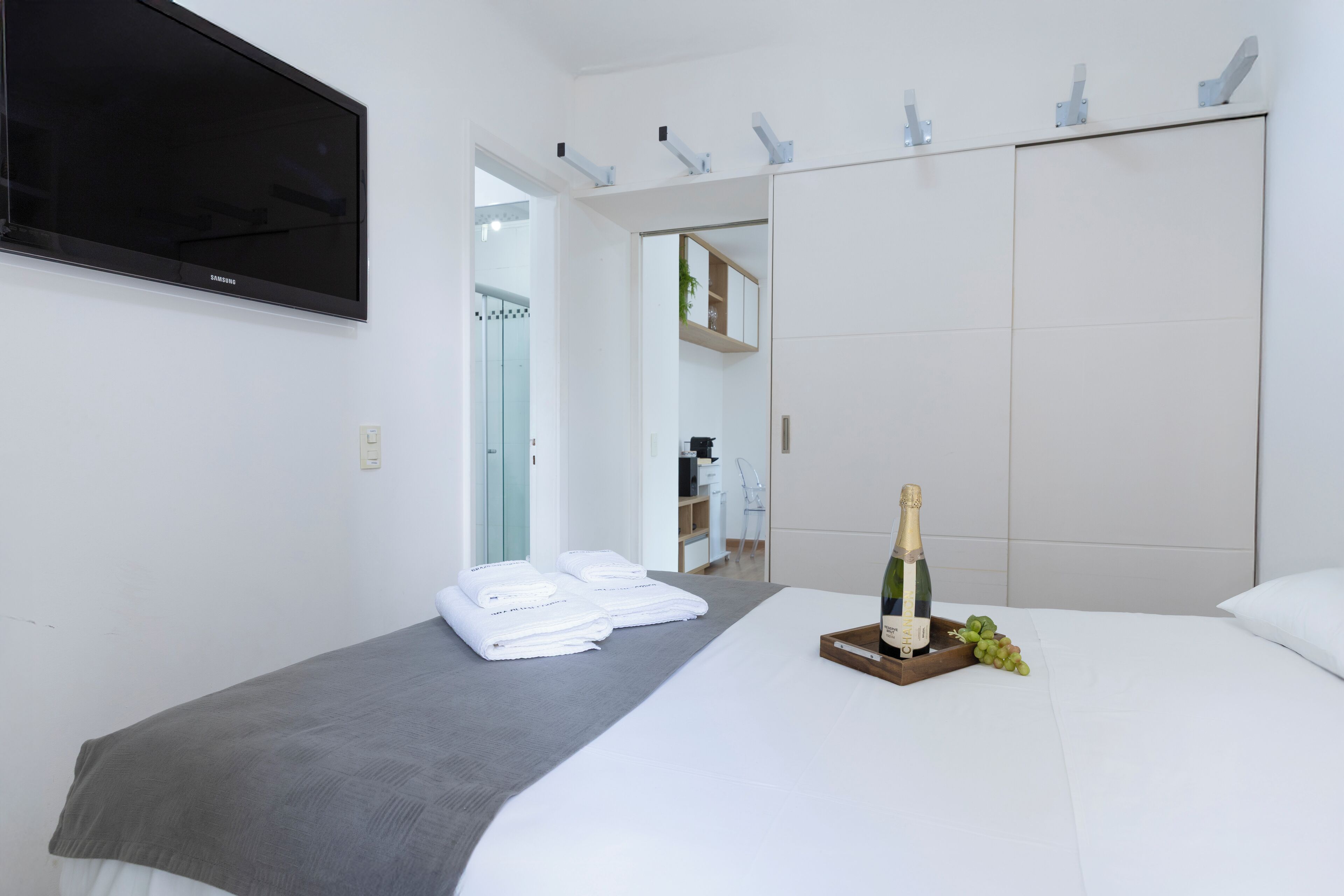 Habitación de hotel con una cama, televisor montado en la pared, armario y una botella de champán sobre la cama.