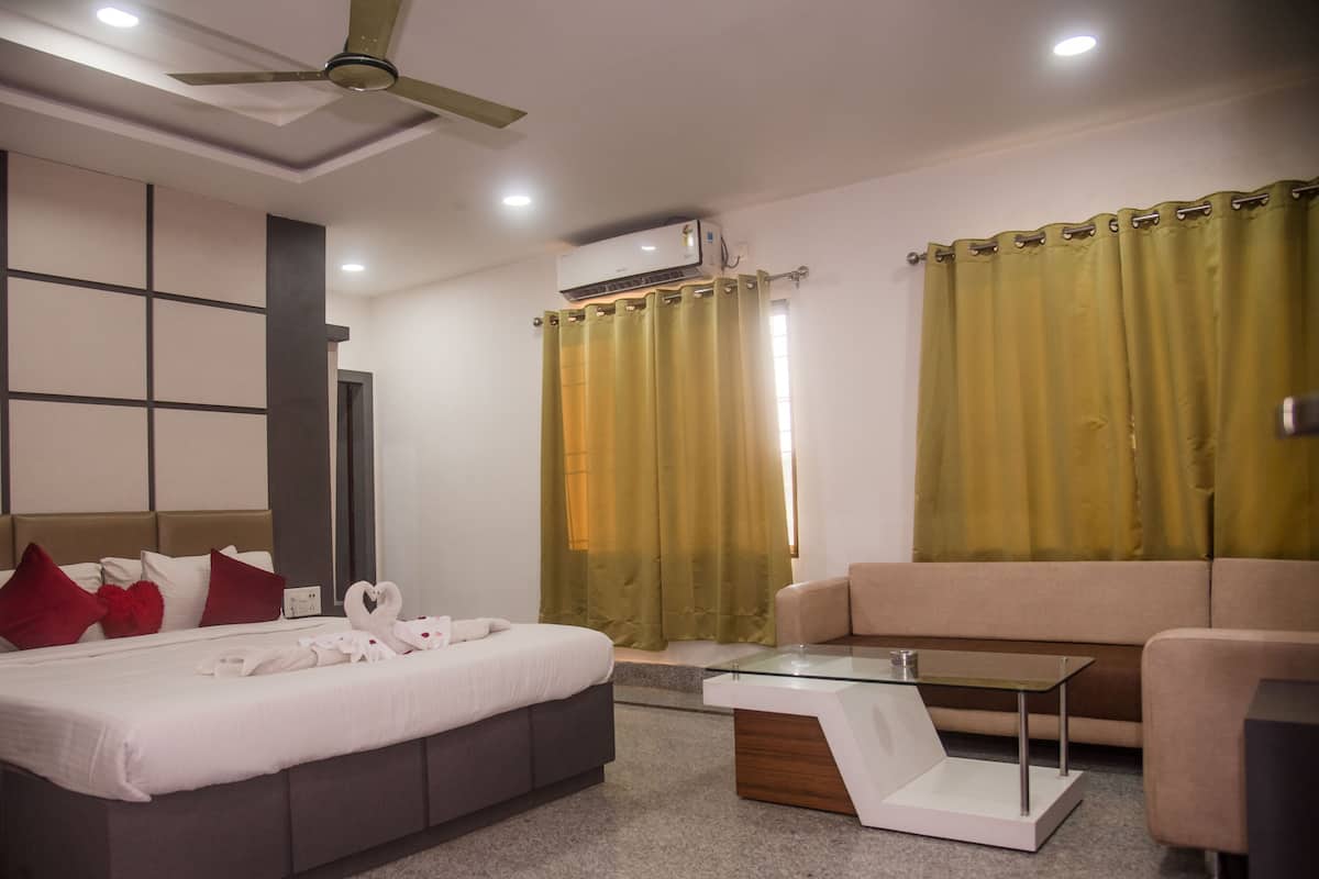 A modern hotel room with a bed, a sofa, a glass coffee table, and a ceiling fan.