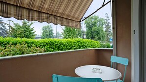 A balcony with a table and chairs, a view of greenery, and a building in the background.