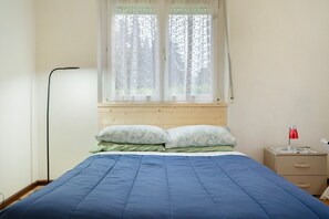 Une chambre à coucher avec un lit, une table de chevet, une lampe et une fenêtre avec des rideaux.