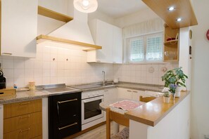Une cuisine avec des meubles blancs, un plan de travail en bois, un évier, une cuisinière et une fenêtre avec des rideaux.