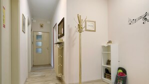A hallway with a floor lamp, a coat rack, a shelf with decorative items, and a welcome mat.