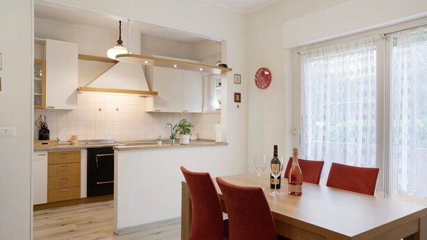 A modern kitchen with wooden cabinets, a dining area with a table and chairs, and a clock on the wall.