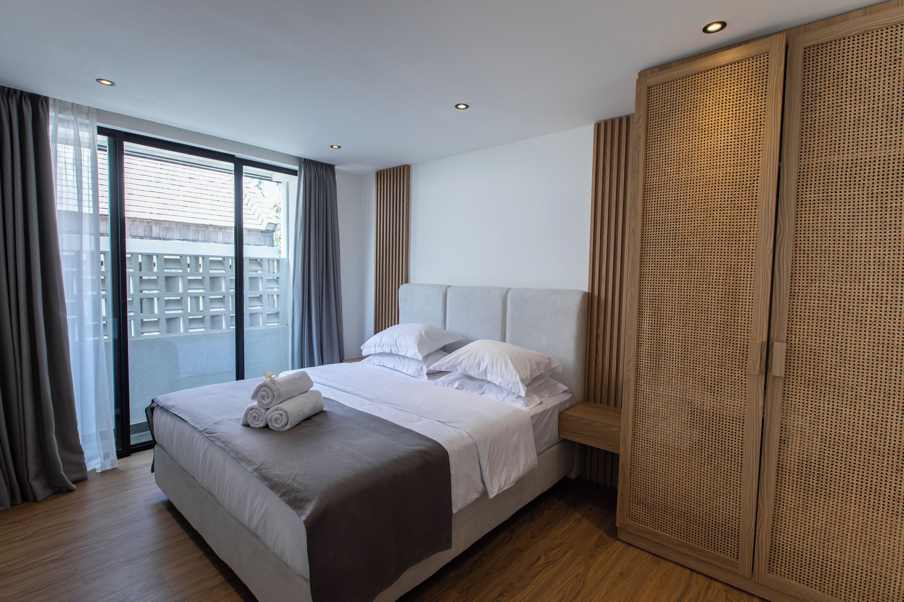 A modern hotel room with a large bed, a wooden wardrobe, and a balcony with a view.