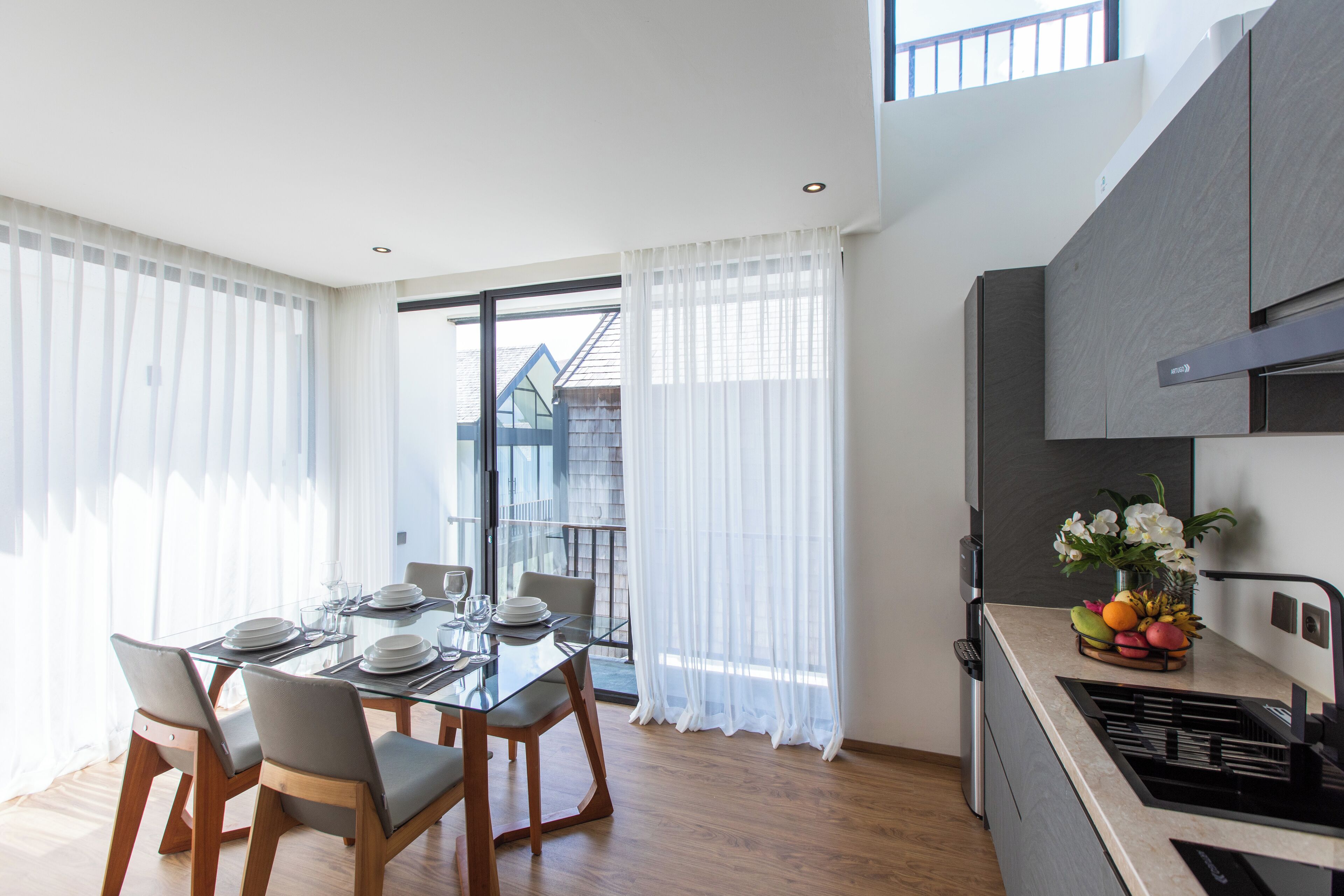A modern kitchen with a dining area, large windows, and a view of a building outside.
