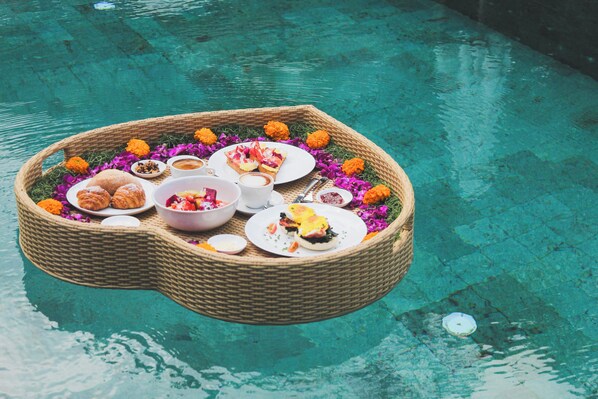 Un montaje flotante para comer con varios platos y flores sobre una piscina transparente.