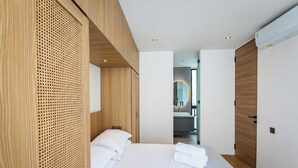 A modern hotel room with a large bed, wooden paneling, and a view into the bathroom.