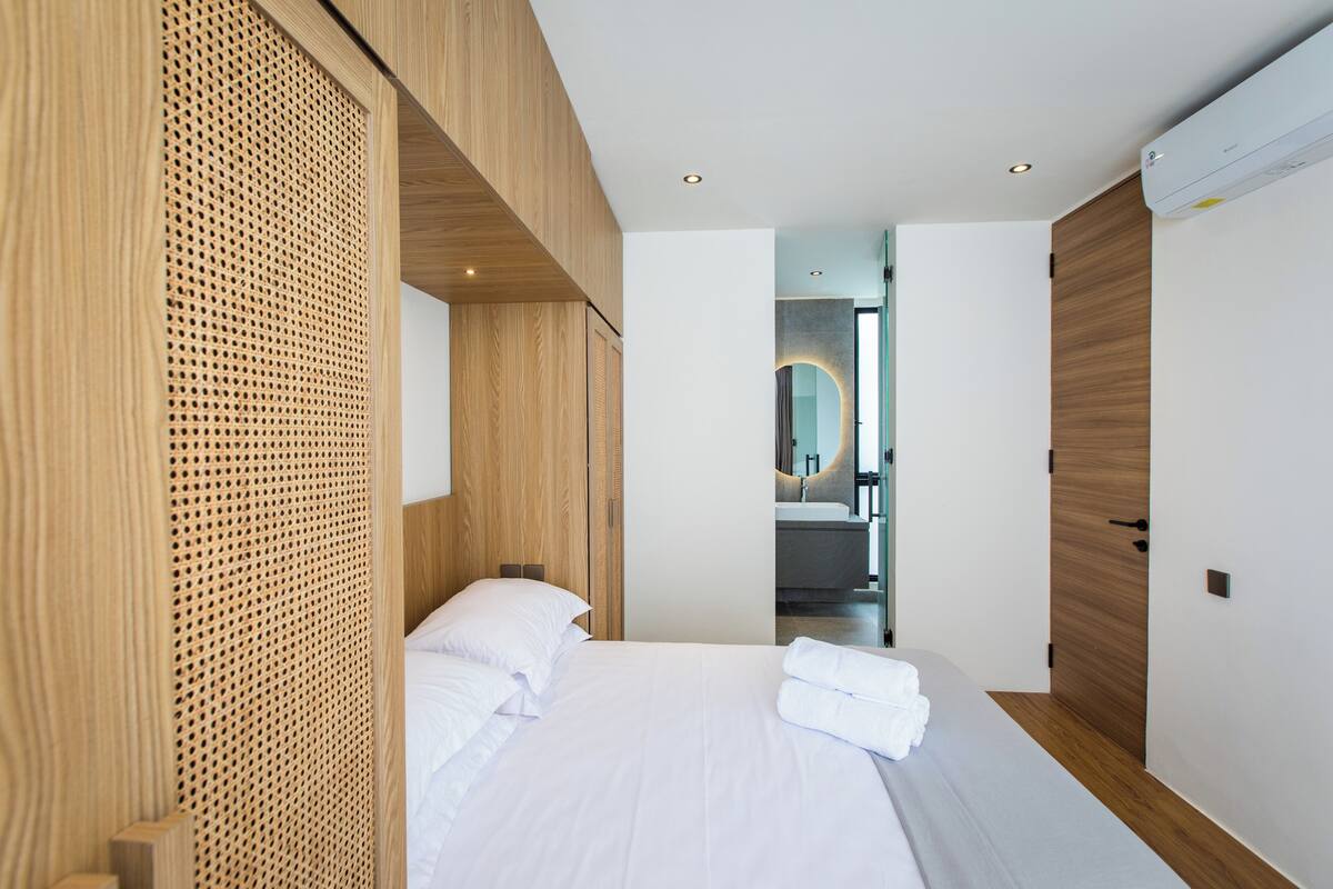 A modern hotel room with a large bed, wooden paneling, and a view into the bathroom.