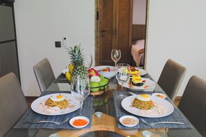 Una mesa de comedor con platos de comida, vasos y un frutero.