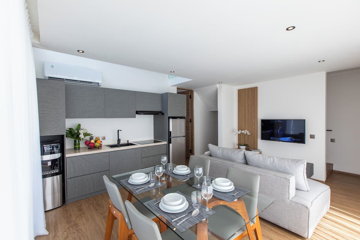 A modern kitchen with grey cabinetry, a built-in oven, and a dining area with a glass table set for four.