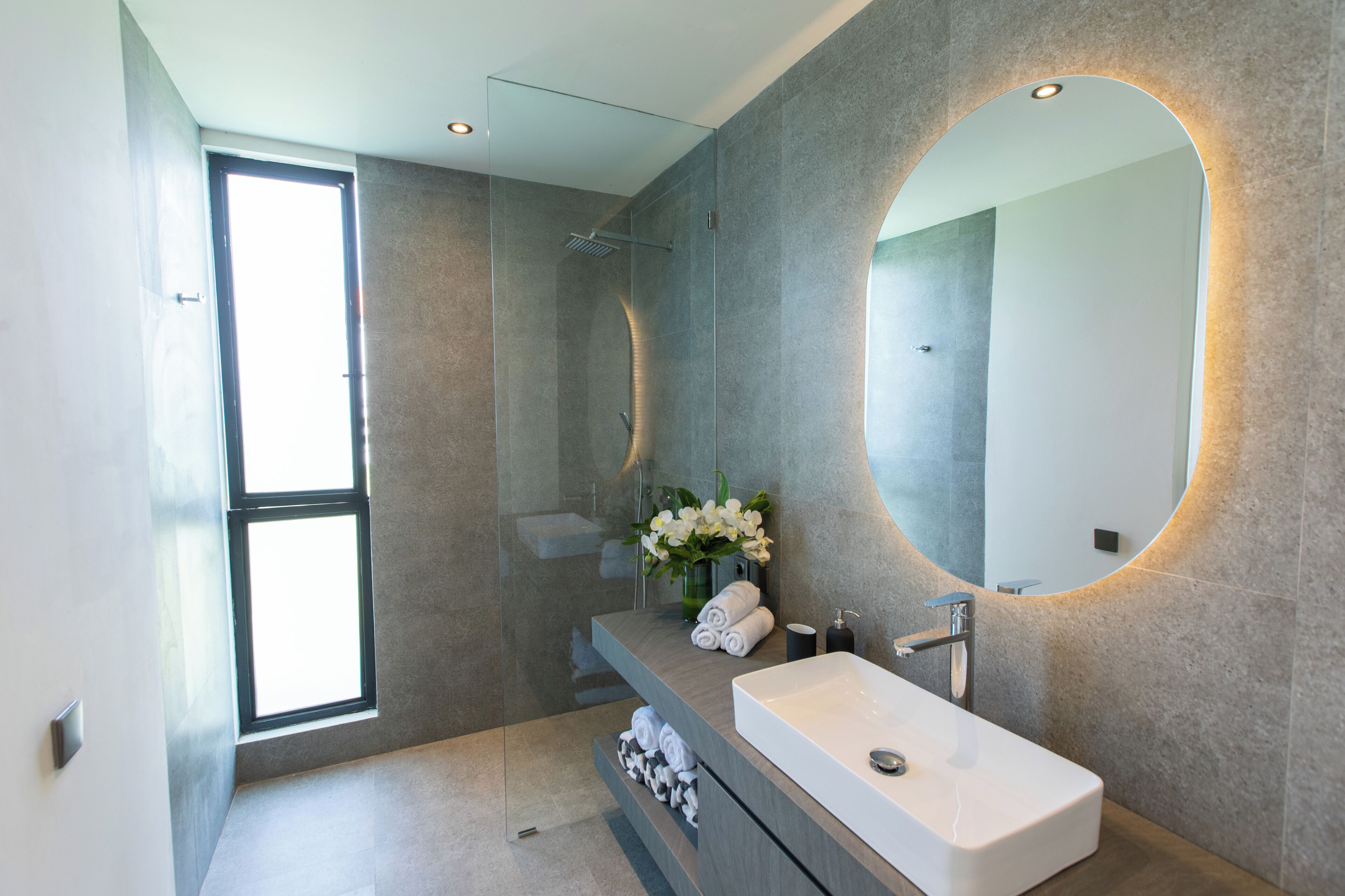 A modern bathroom with a large window, a rectangular sink, and a mirror with a curved frame.