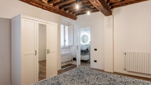 A bedroom with a patterned bedspread, a wardrobe, a mirror, and a ceiling with exposed wooden beams.