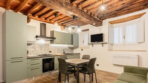A compact kitchen with a dining area, wooden ceiling beams, and a flat-screen TV.