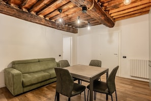 Ein Zimmer mit Holzboden, einem grünen Sofa, einem Holztisch und vier Stühlen.