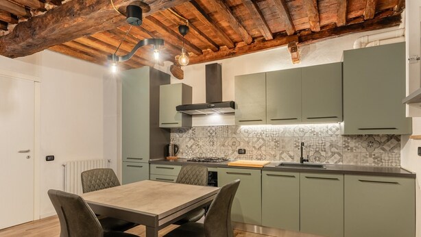 A modern kitchen with green cabinets, a wooden dining table, and a tiled backsplash.