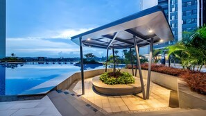Un área de piscina moderna al aire libre, con una zona de estar cubierta y vistas al horizonte de la ciudad.
