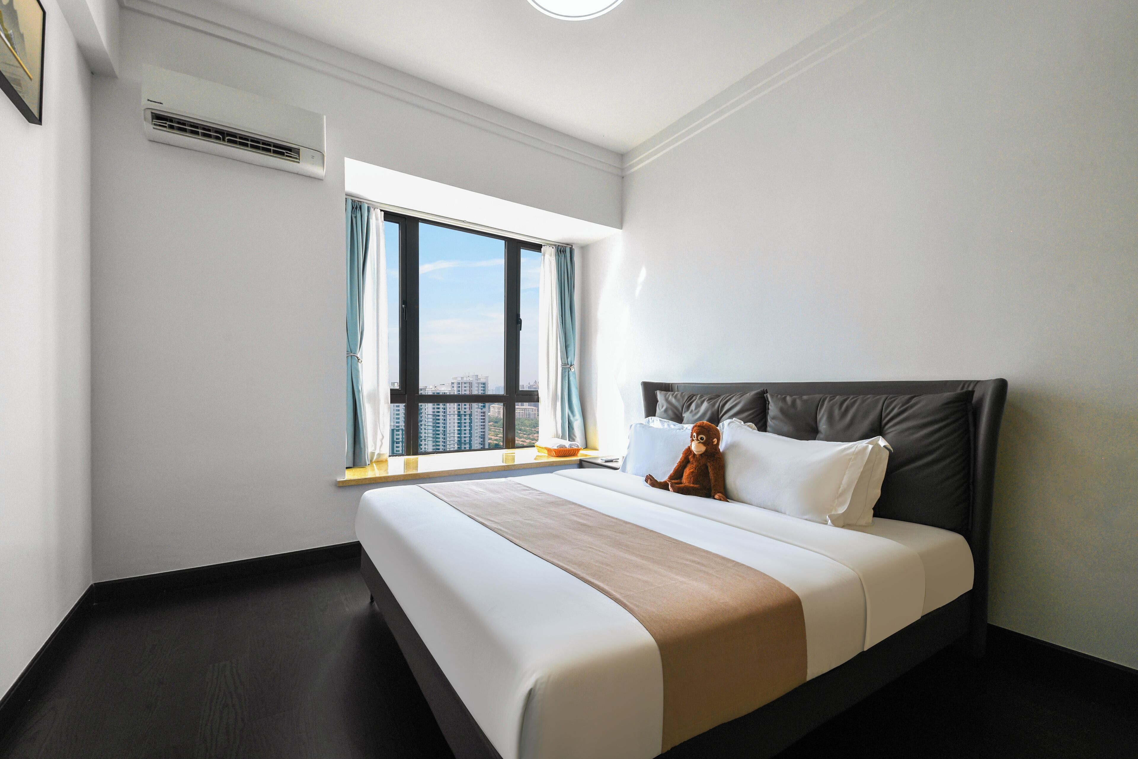 Habitación de hotel con una cama grande, una ventana con cortinas, vistas a la ciudad y un equipo de aire acondicionado en la pared.