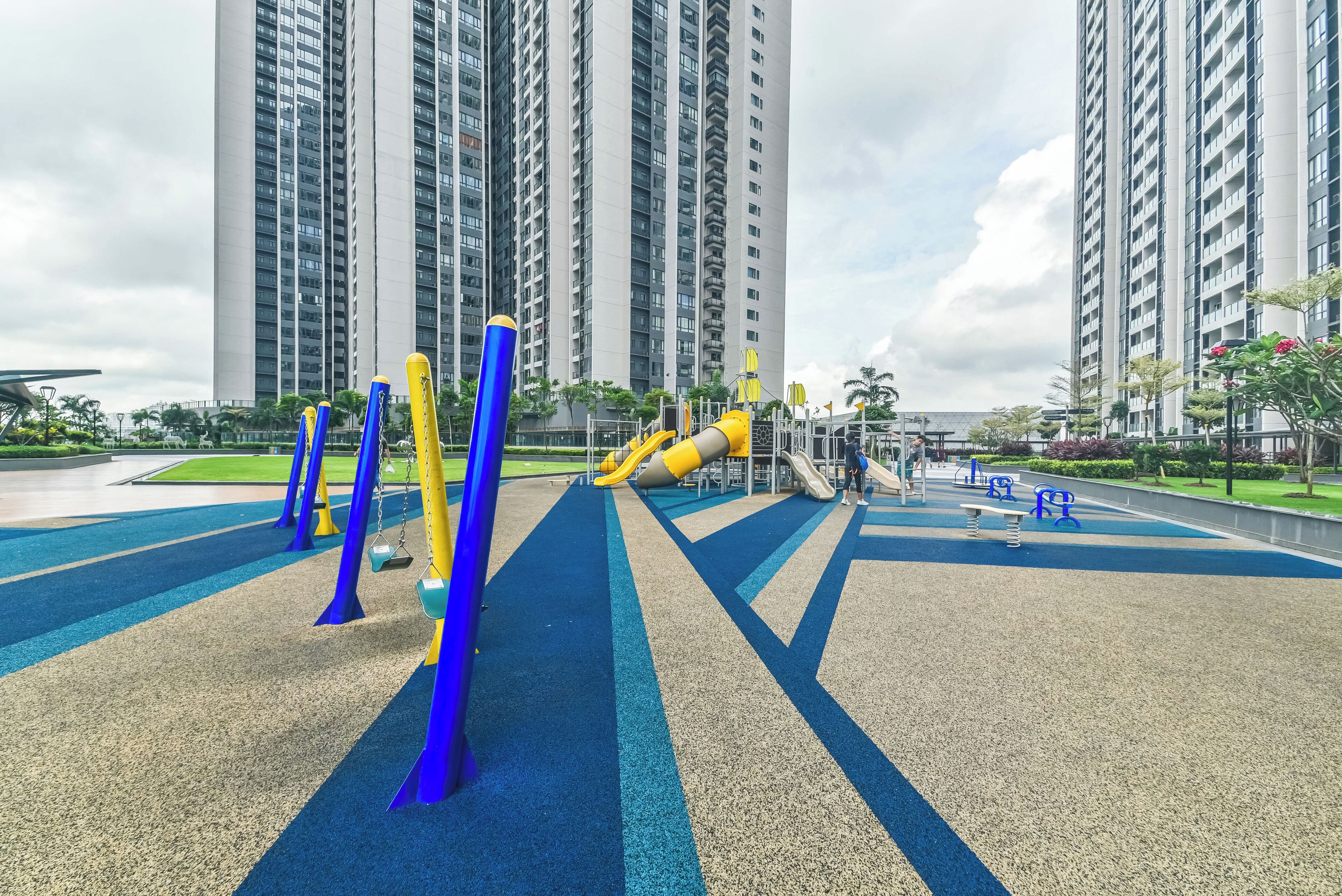 Un parque infantil con columpios y toboganes, rodeado de edificios residenciales altos.