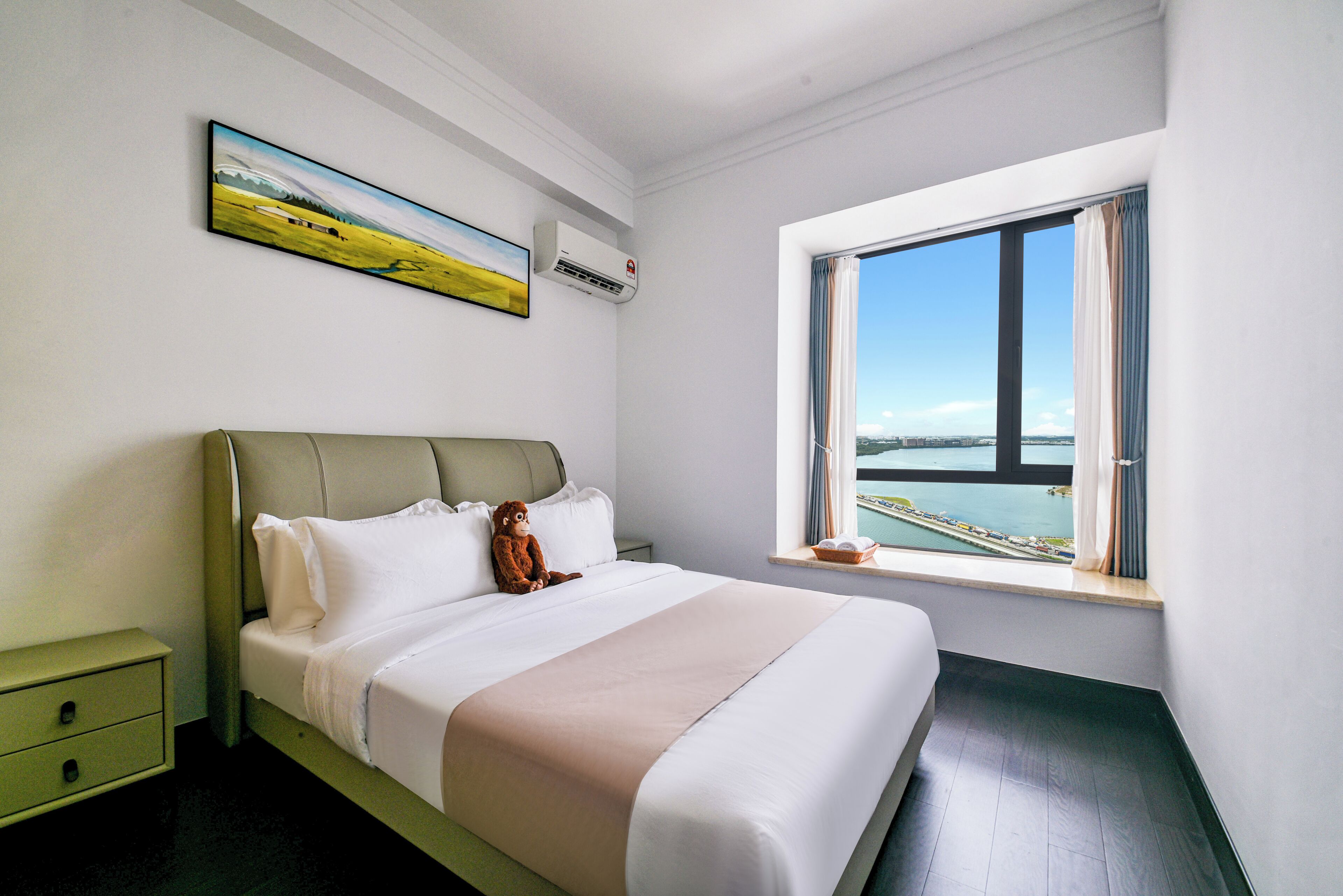 A neatly made bed with a view of a body of water through a large window.