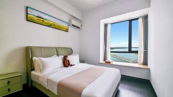 A neatly made bed with a view of a body of water through a large window.