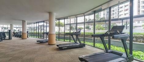 A gym with treadmills, exercise bikes, and a large window overlooking a cityscape.
