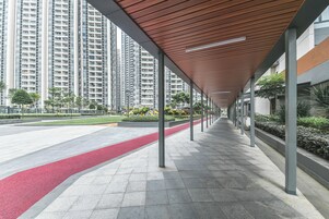 A covered walkway with a red bike lane, tall residential buildings, and greenery in the background.
