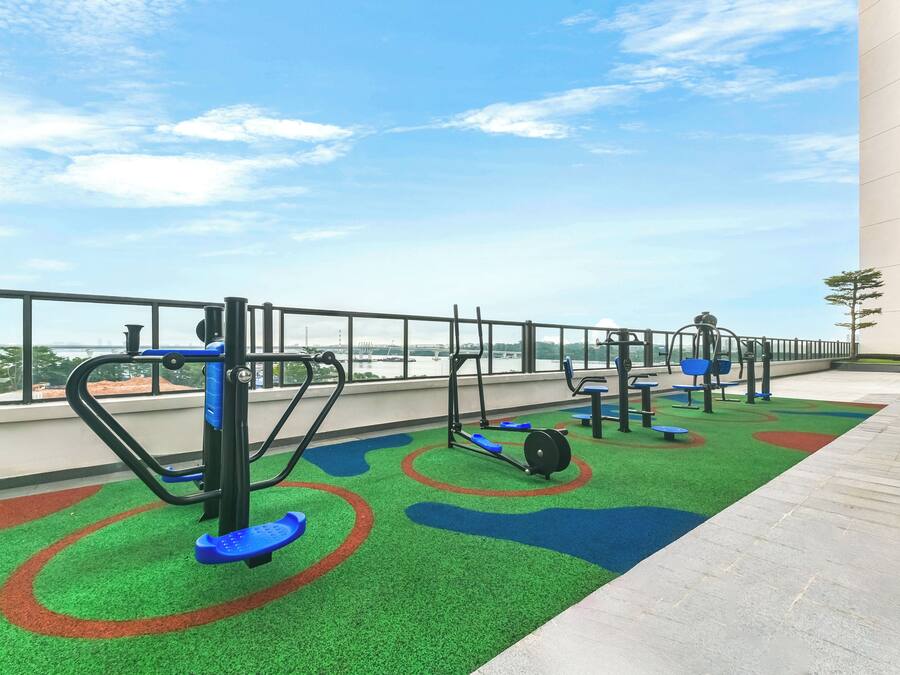 An outdoor gym area with exercise equipment, green artificial turf, and a view of a bridge.