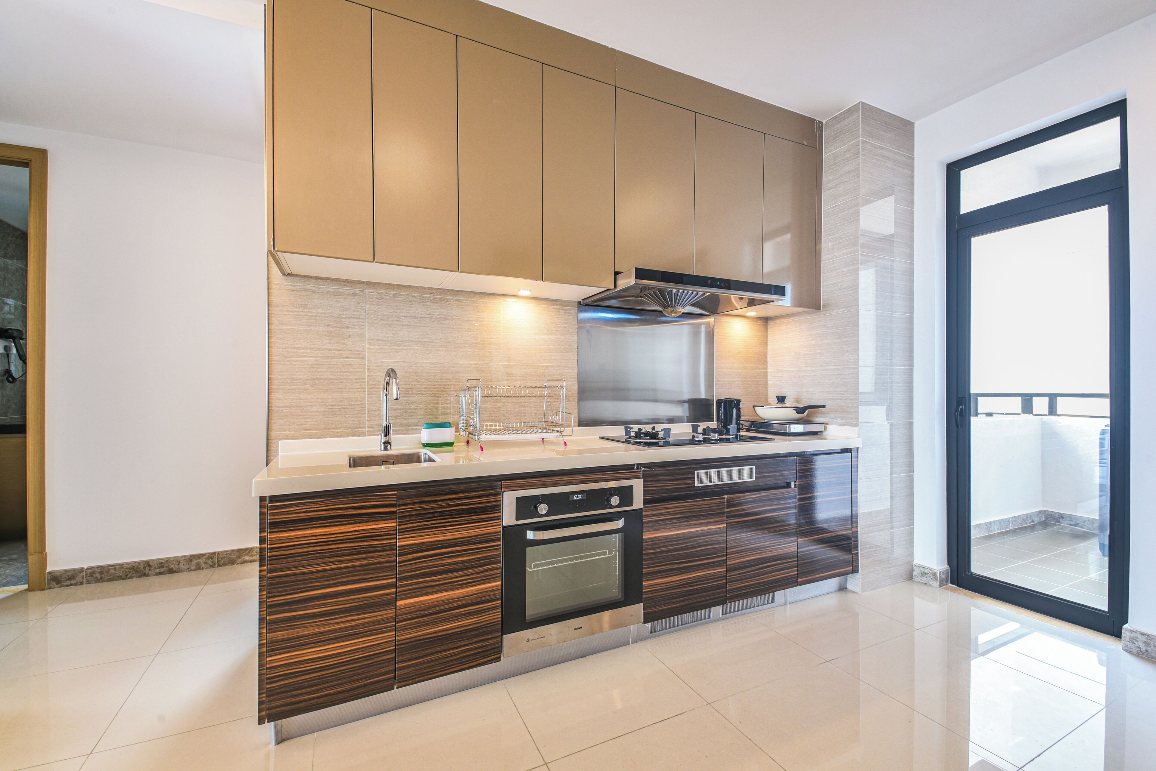 A modern kitchen with a built-in oven, a stainless steel range hood, and a large window providing natural light.