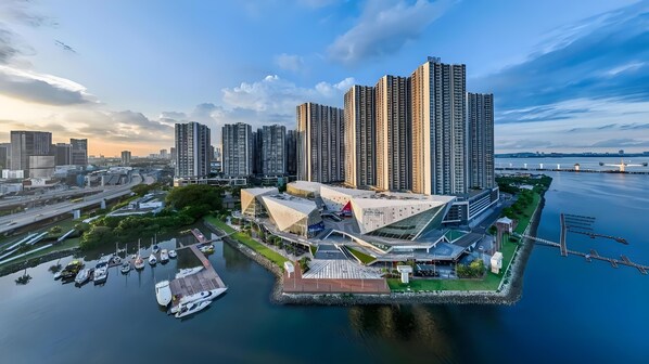 Una zona urbana frente al mar con edificios altos, un puerto deportivo con barcos y un edificio moderno distintivo con un diseño de techo único.