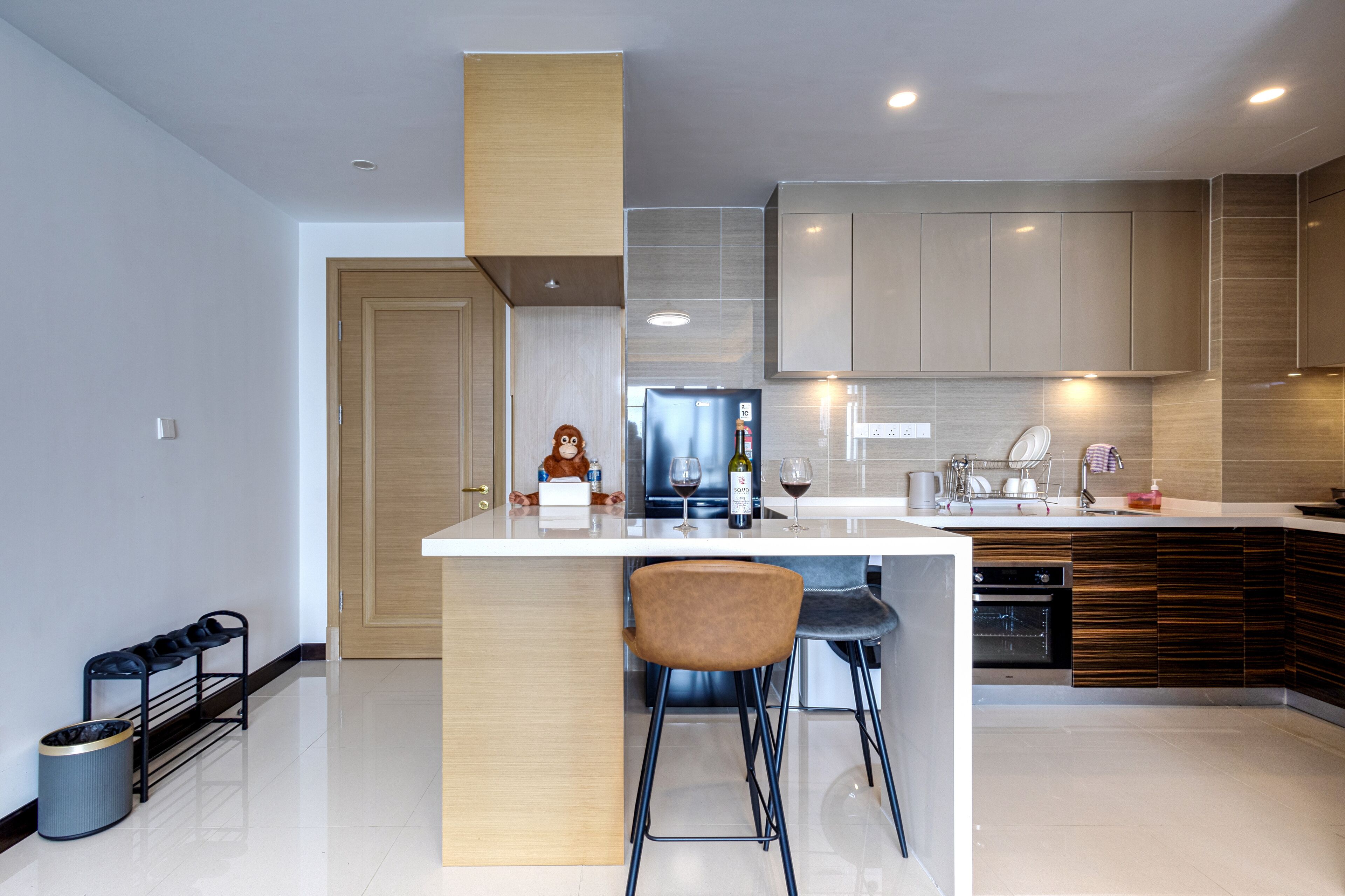 A modern kitchen with a central island, bar stools, a built-in oven, and a wine bottle.