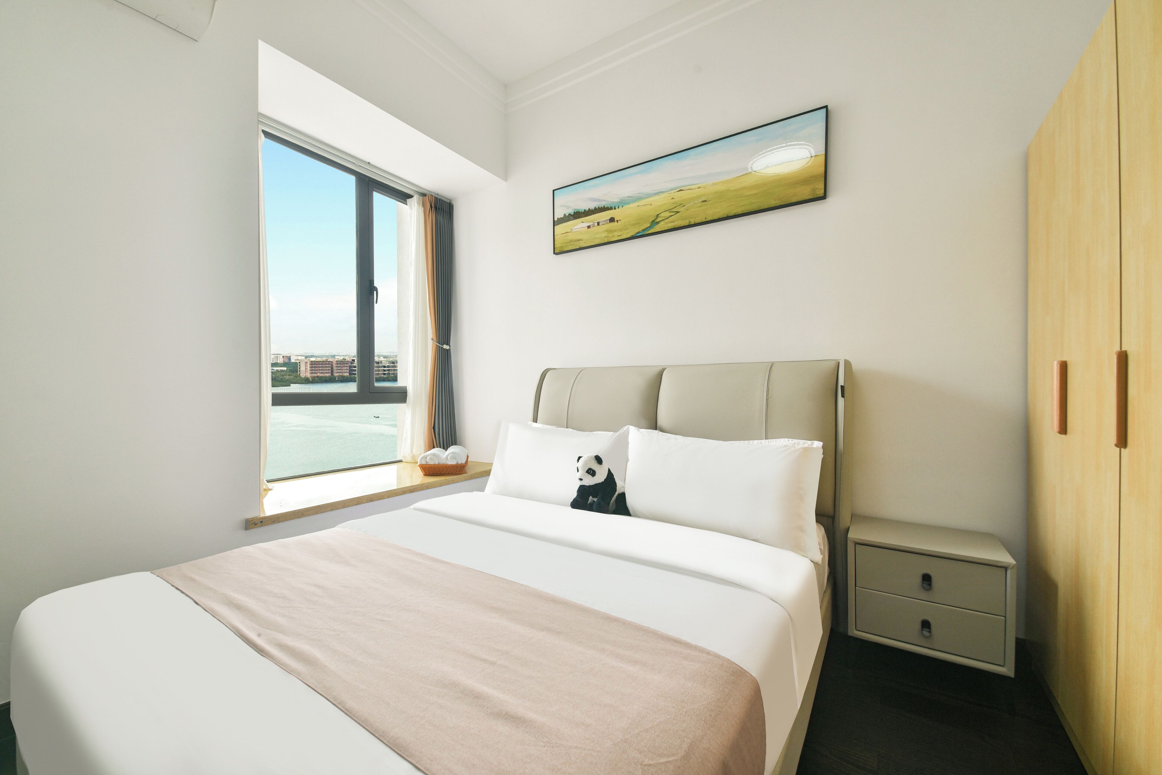 Ein Schlafzimmer mit einem großen Bett, einem Nachttisch, einem Holzschrank, einem Fenster mit Blick auf Gebäude und einem Bild an der Wand.