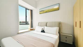 Ein Schlafzimmer mit einem großen Bett, einem Nachttisch, einem Holzschrank, einem Fenster mit Blick auf Gebäude und einem Bild an der Wand.