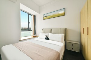 Ein Schlafzimmer mit einem großen Bett, einem Nachttisch, einem Holzschrank, einem Fenster mit Blick auf Gebäude und einem Bild an der Wand.