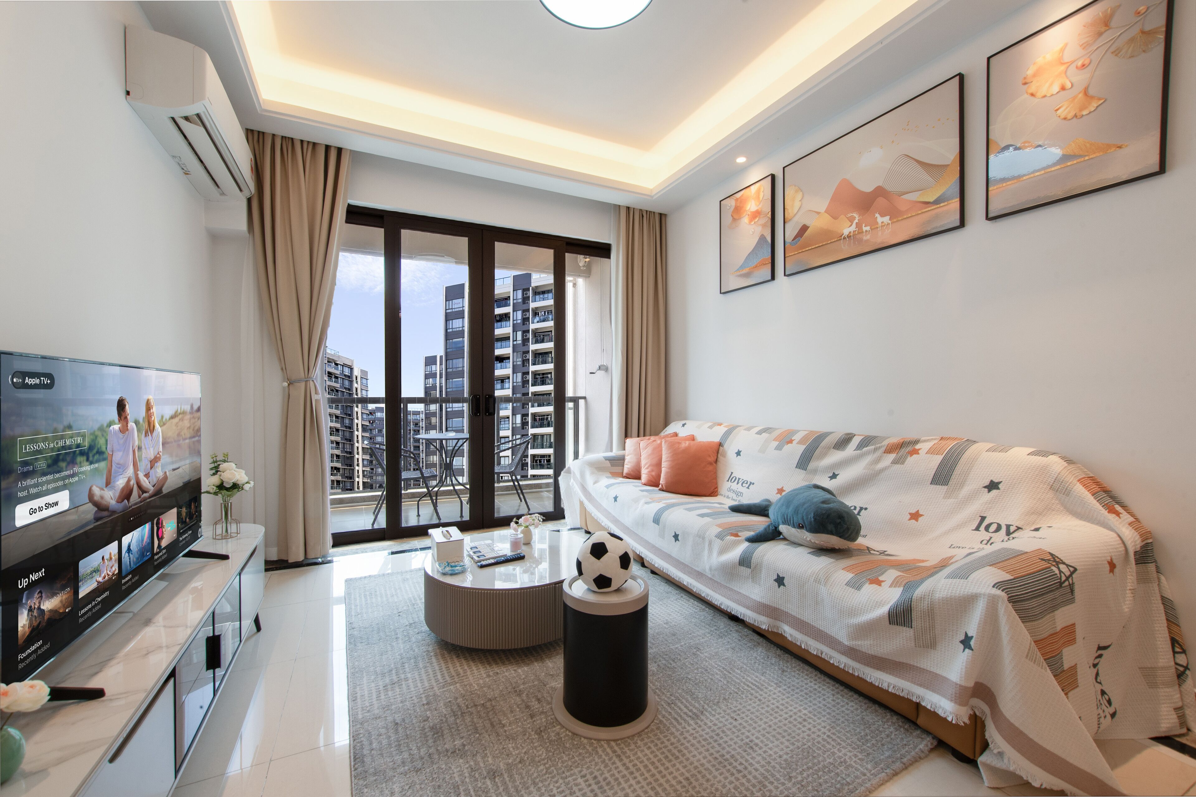 Una sala de estar moderna con una televisión de pantalla plana, un sofá, una mesa de centro y vistas de la ciudad a través de amplios ventanales.