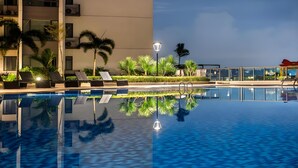 Una piscina con sillas de descanso y palmeras, rodeada por un edificio con ventanas amplias y vistas al mar.