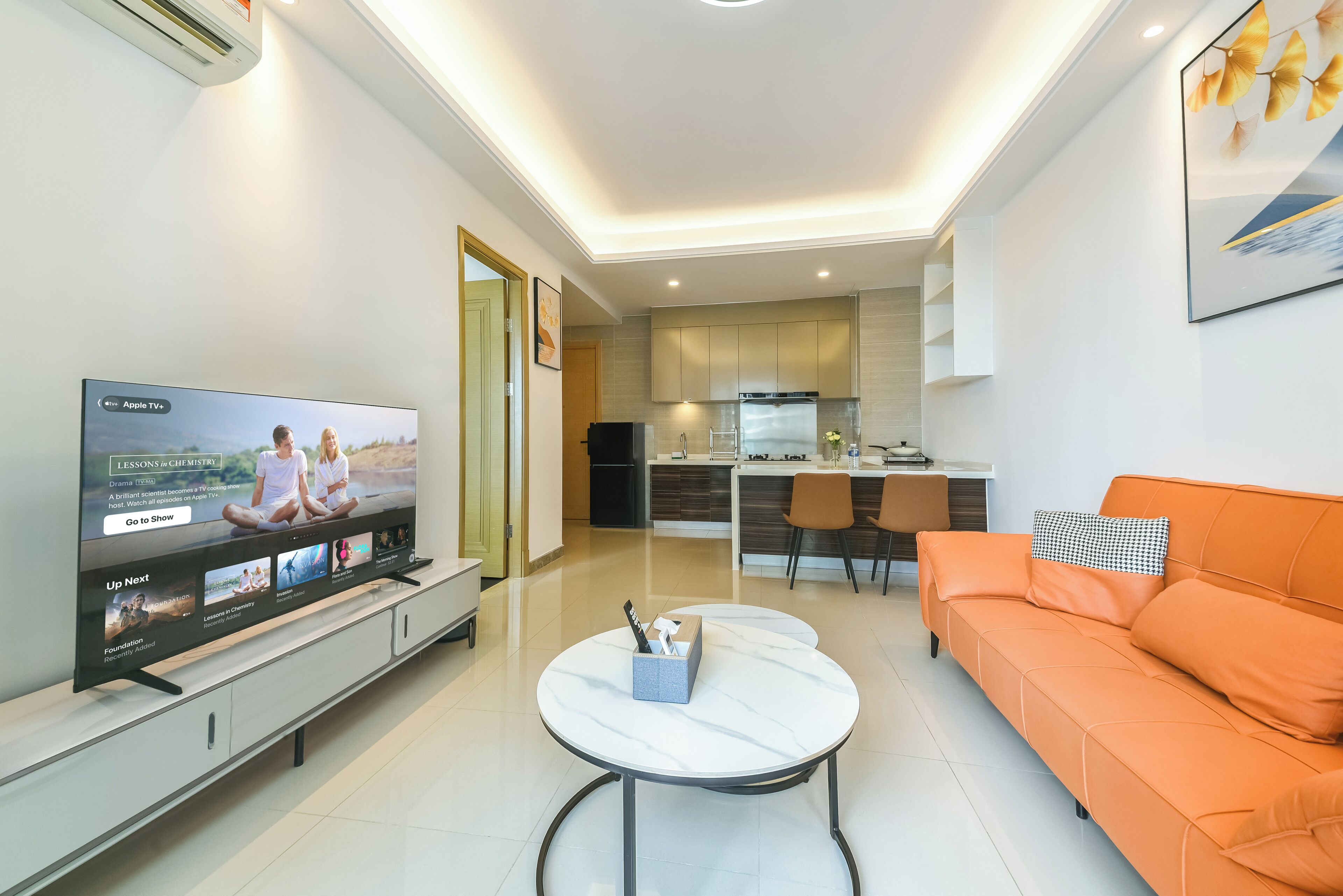 A modern living room with a flat-screen TV, a white coffee table, and an orange sofa.