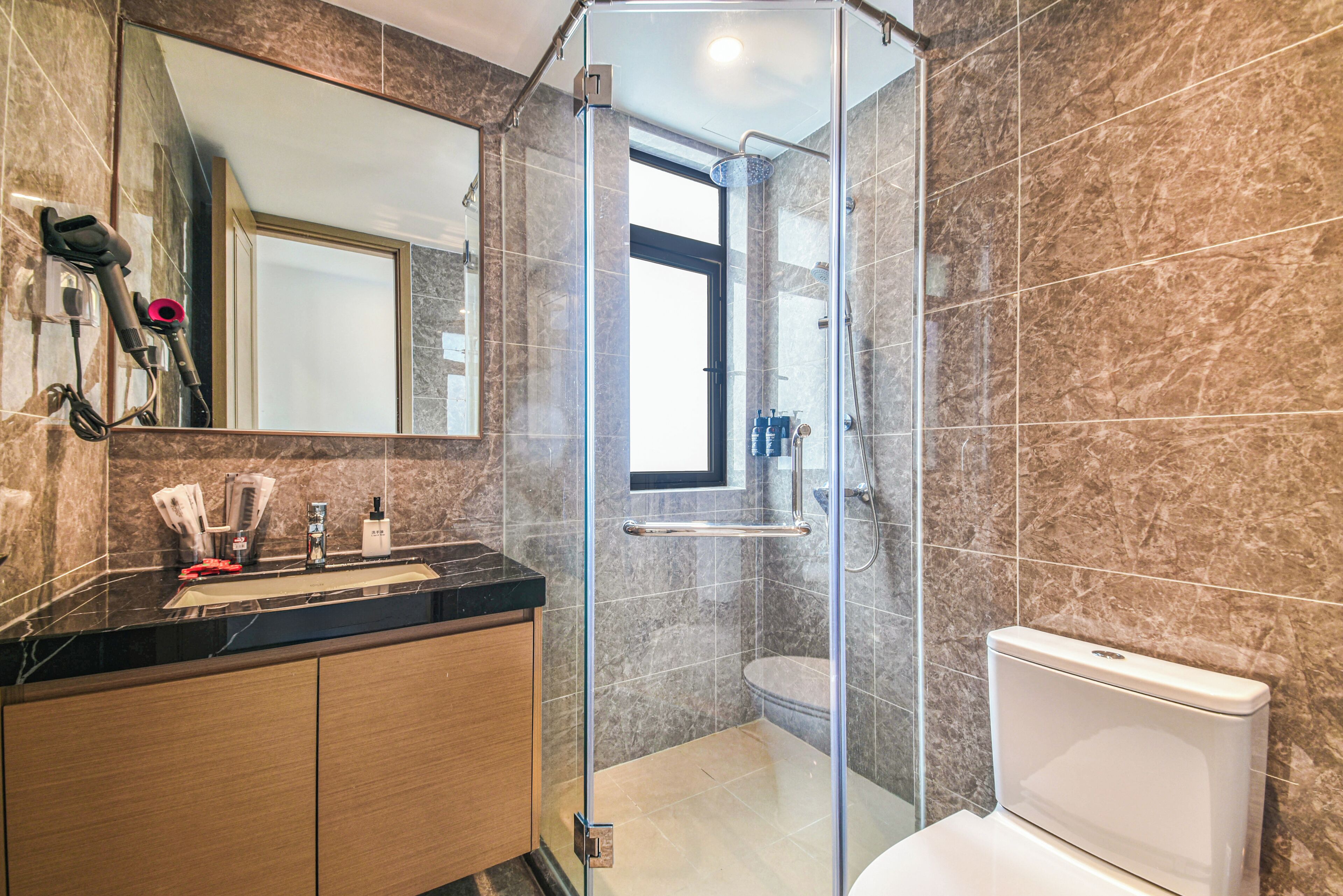 A modern bathroom with a glass-enclosed shower, a vanity with a black countertop, and a toilet.