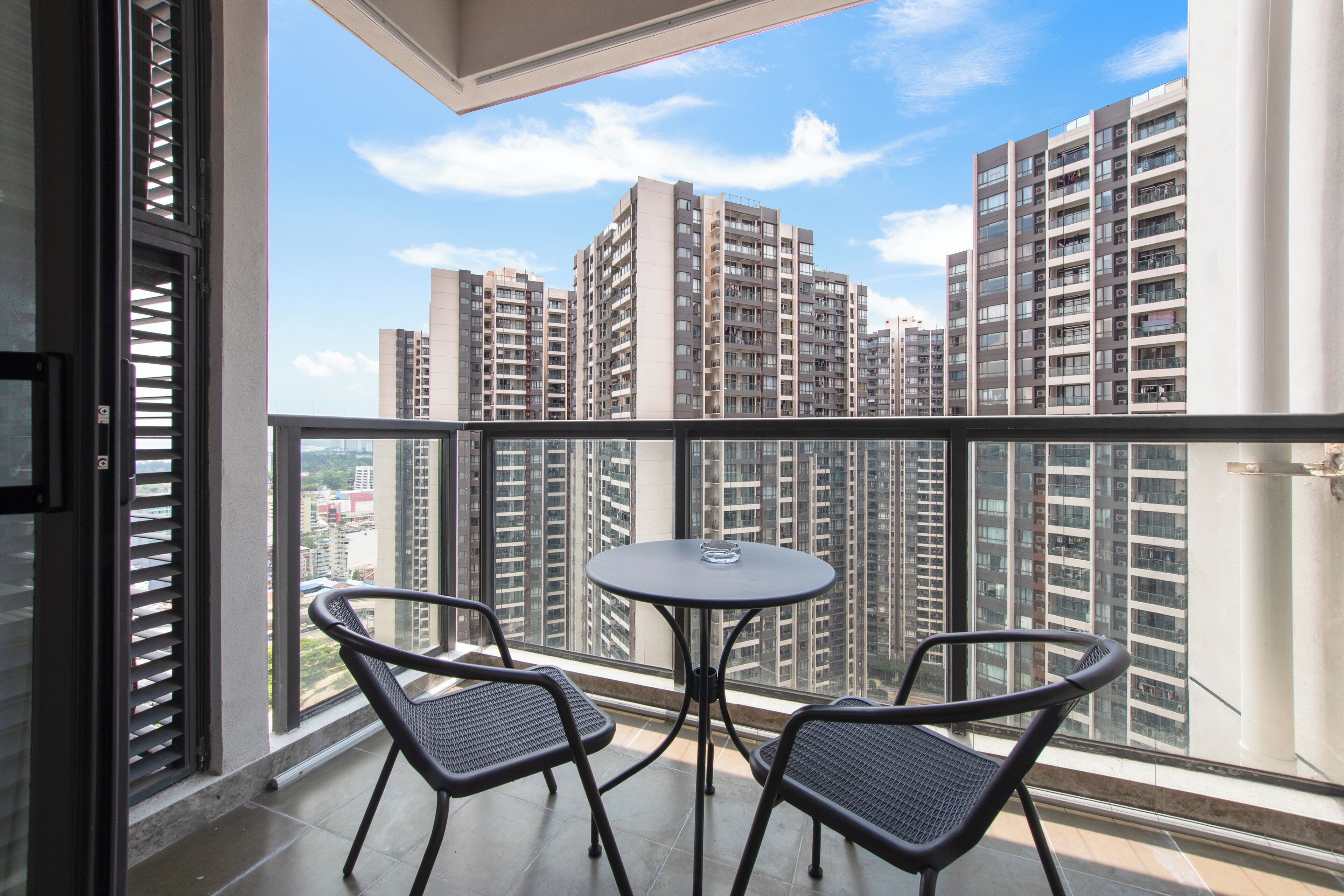 Un balcón con dos sillas y una mesa, con vistas a un paisaje urbano con edificios altos.
