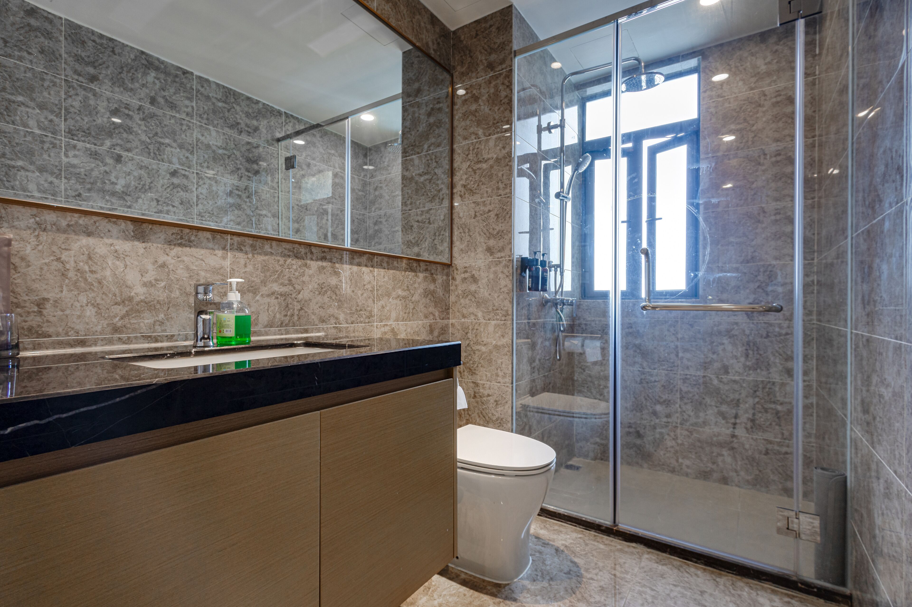 A modern bathroom with a marble countertop, a glass shower enclosure, and a toilet.