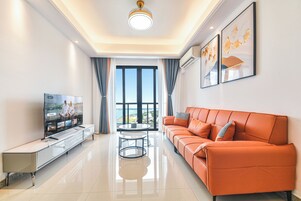 A modern living room with a sofa, TV, and a view through a large window.