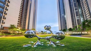 Una escultura moderna en un área verde con edificios altos al fondo.