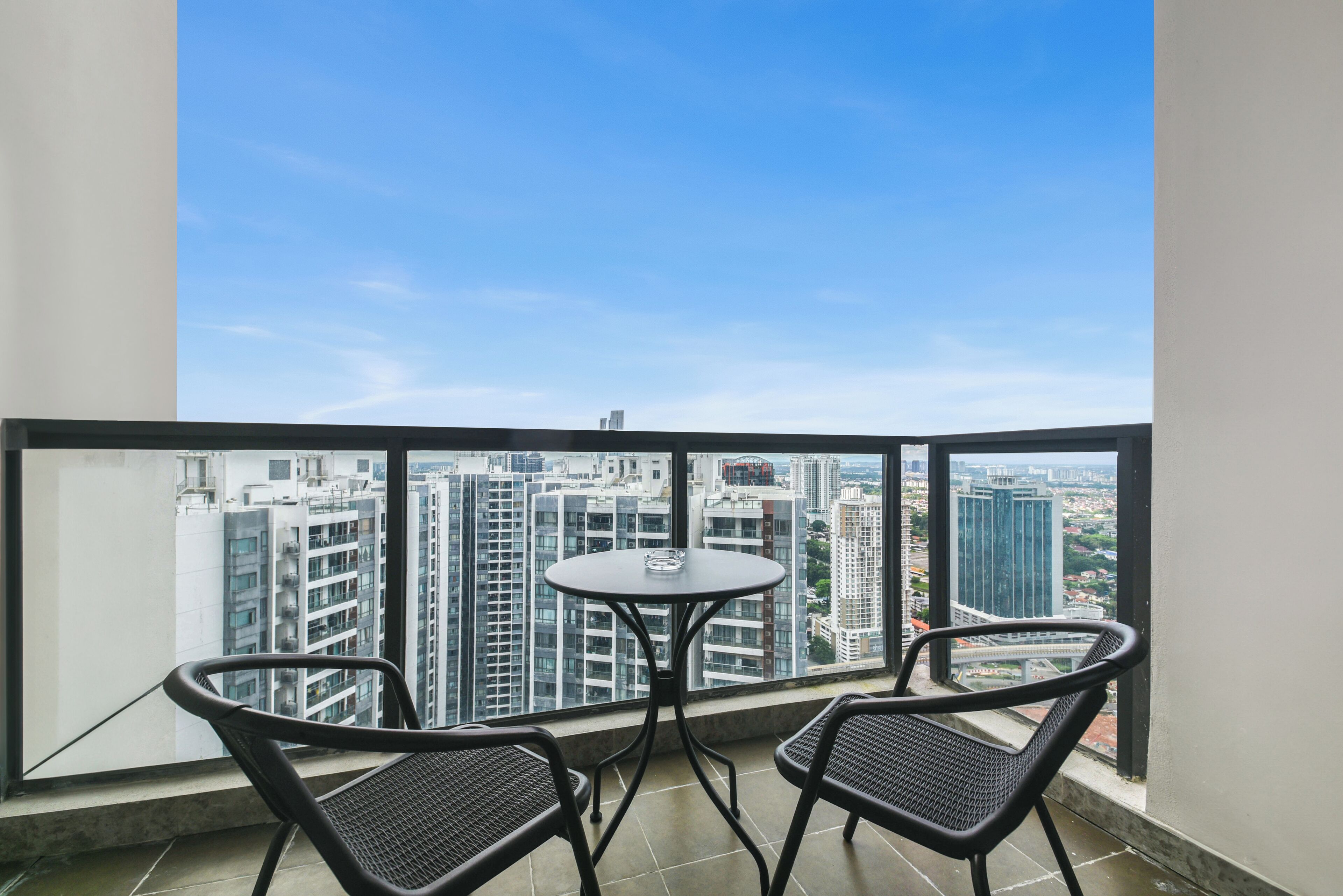 A balcony with a table and two chairs, offering a view of a cityscape with high-rise buildings.