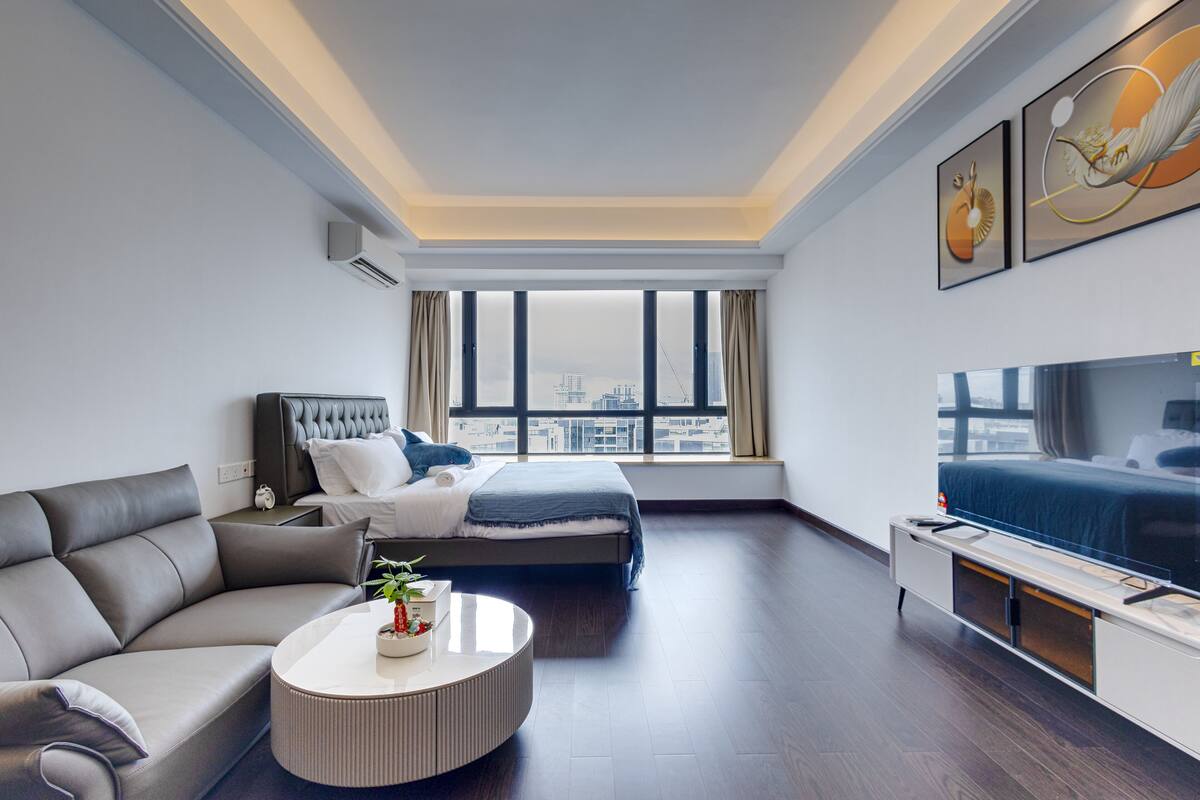 A modern hotel room with a bed, sofa, TV, and a city view.