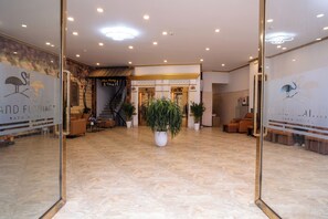A hotel lobby with a marble floor, potted plants, and a reception desk.