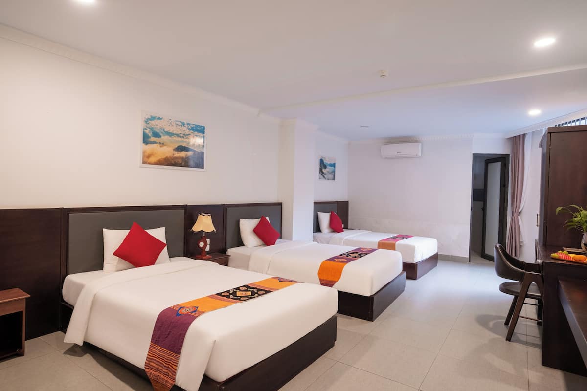 Habitación de hotel con tres camas, un escritorio y una silla.